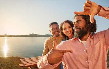Actor portrayal of TUKYSA (tucatinib) patient and loved ones standing by a lake at sunset, the man framing a photo of themselves with his hands, representative of the TUKYSA (tucatinib) logomark.