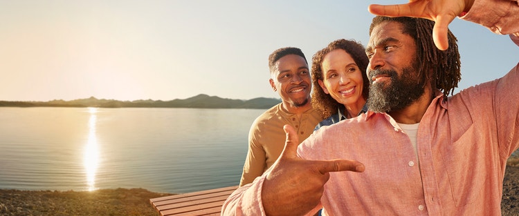 Actor portrayal of TUKYSA (tucatinib) patient and loved ones standing by a lake at sunset, the man framing a photo of themselves with his hands, representative of the TUKYSA (tucatinib) logomark.